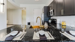 A modern kitchen with dark cabinets, a black granite countertop, and a gold faucet.
