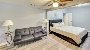 Un dormitorio con cama, sofá, dos lámparas, ventilador de techo y una puerta.