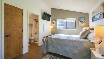 A bedroom with a bed, a nightstand, a TV mounted on the wall, and a window.