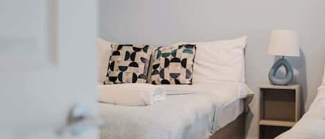 A bedroom with a bed, pillows, a bedside table, and a lamp.