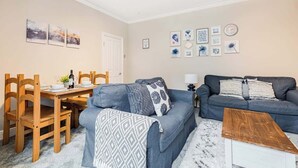 A living room with a sofa, a coffee table, a dining table with chairs, and wall art. - Spacious 3 Bedroom House Sleeps 6 With WiFi (Bedford)