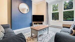 A living room with a TV, a round mirror, a coffee table, and a sofa. - Spacious 3 Bedroom House Sleeps 6 With WiFi (Bedford)
