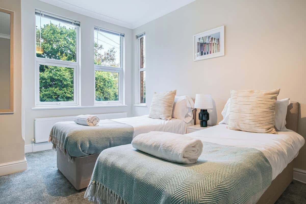 A bedroom with two beds, a window with a view of greenery, and a framed picture on the wall.