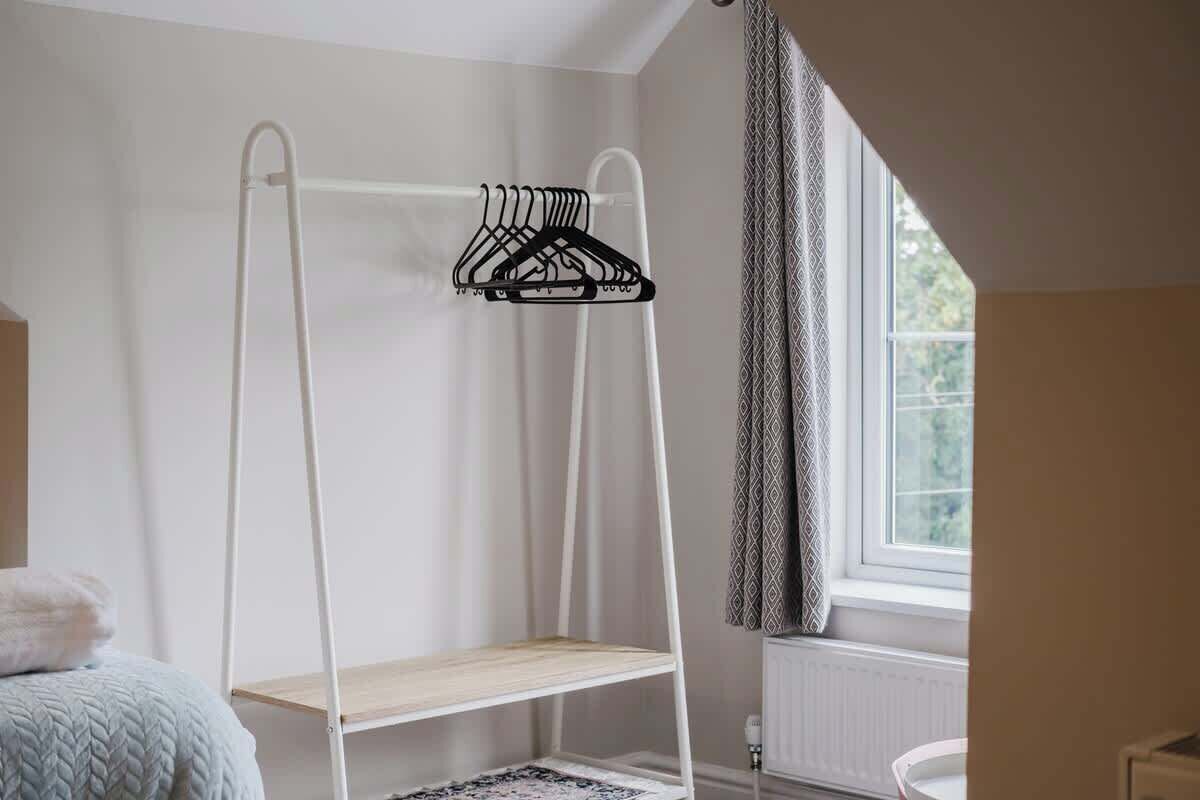Ein Stockbett mit weißem Metallgestell und einem Holzregal, ein Teppich mit Muster sowie ein Fenster mit Vorhängen.