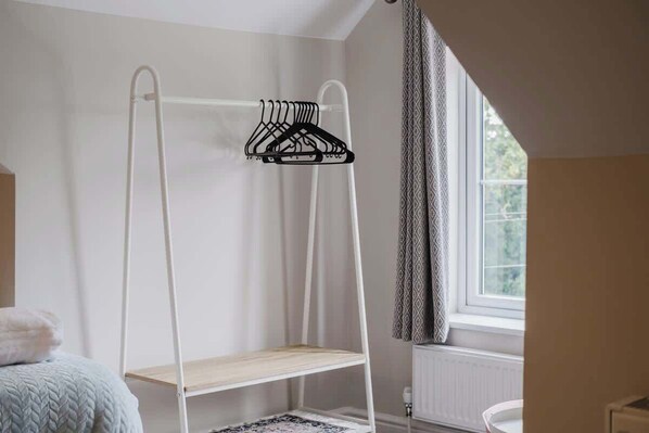 A bunk bed with a white metal frame and a wooden shelf, a patterned rug, and a window with curtains.