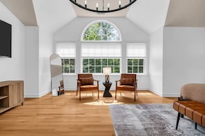 A spacious room with a high ceiling, large windows, a wooden floor, two leather chairs, a sofa, a mirror, and a lamp. - Group Spring Retreat | Fun Games & Gourmet Kitchen (Airmont)