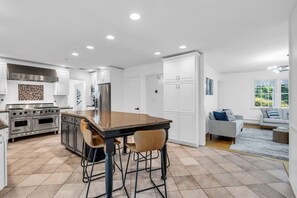 Una cocina moderna con una isla central, electrodomésticos de acero inoxidable y un comedor con taburetes de bar.