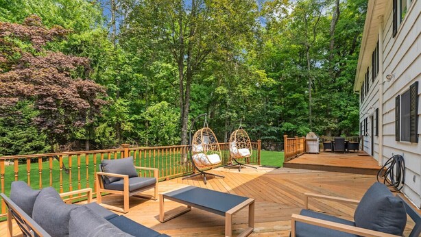 Eine Holzterrasse mit Gartenmöbeln, einem Schaukelstuhl und Blick auf ein Haus.