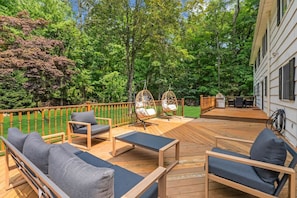 Terraza de madera con mobiliario exterior, una silla colgante y vista a una casa.