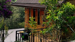 A wooden cabin with a metal roof, surrounded by lush greenery and a view of a forested hill. - Chahill Dalat (Xuan Truong - Da Lat)