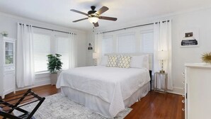 Ein Schlafzimmer mit einem großen Bett, weißen Vorhängen, einem Deckenventilator und einer kleinen Topfpflanze.