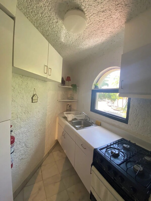 Een kleine keuken met witte kastjes, een gasfornuis, een spoelbak en een raam met uitzicht.