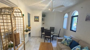 A living room with a wooden coffee table, beige sofas, a dining table with chairs, a ceiling fan, and a window with a view. - Villa with pool in hotel zone (Cancún)
