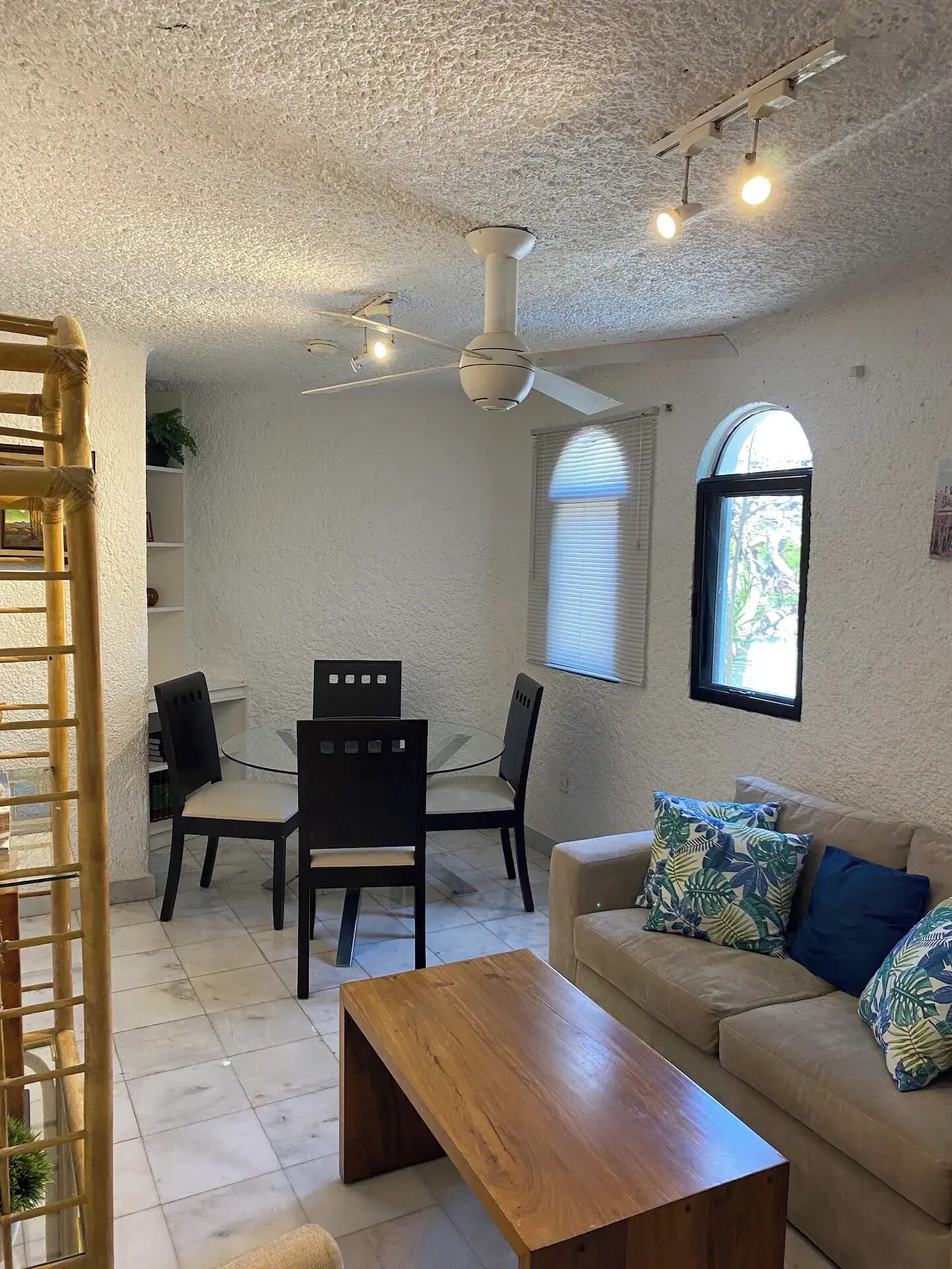 A compact living space with a dining area, a sofa, a wooden coffee table, and a ceiling fan.
