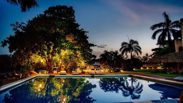 A poolside area with lounge chairs, a large tree, and a thatched-roof structure. - Villa with pool in hotel zone (Cancún)