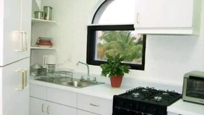 A compact kitchen with white cabinets, a sink, a stove, and a window with a plant. - Villa with pool in hotel zone (Cancún)