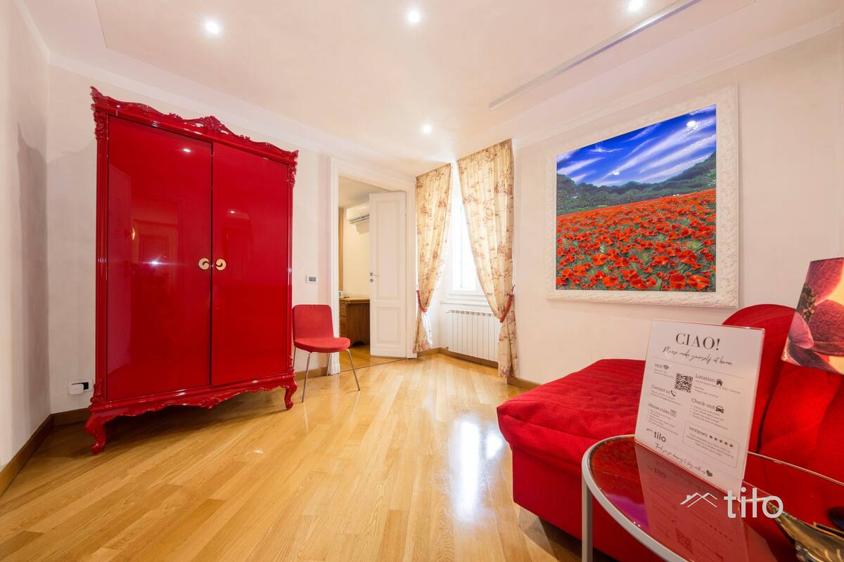 A room with a red wardrobe, a red sofa, a glass coffee table, and a painting of a field of red flowers.