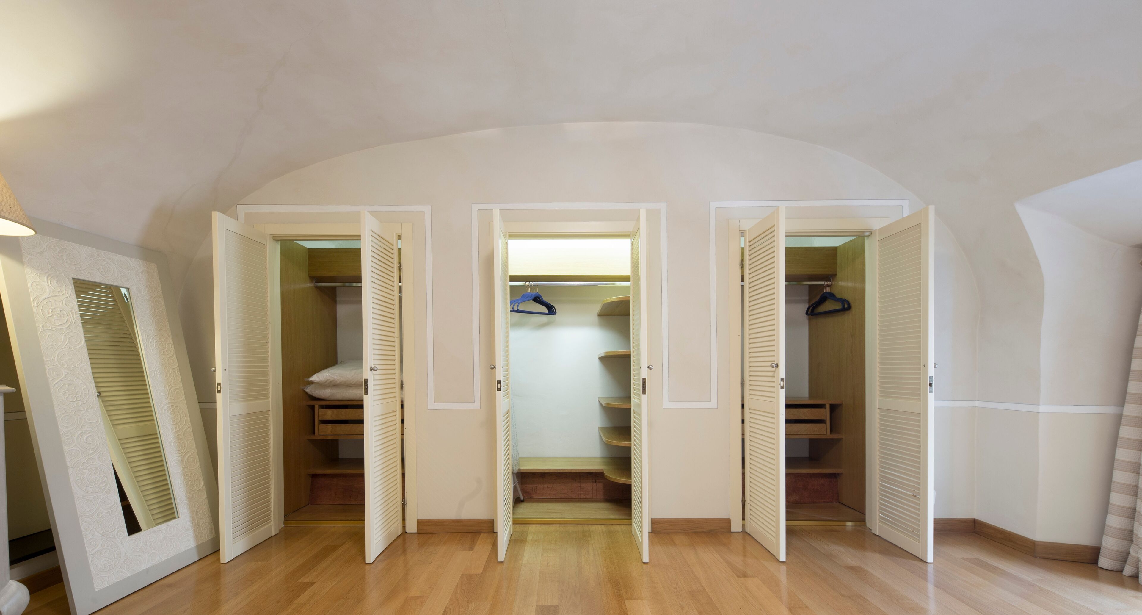 A room with a wooden floor, a white door with a mirror, and a closet with sliding doors.
