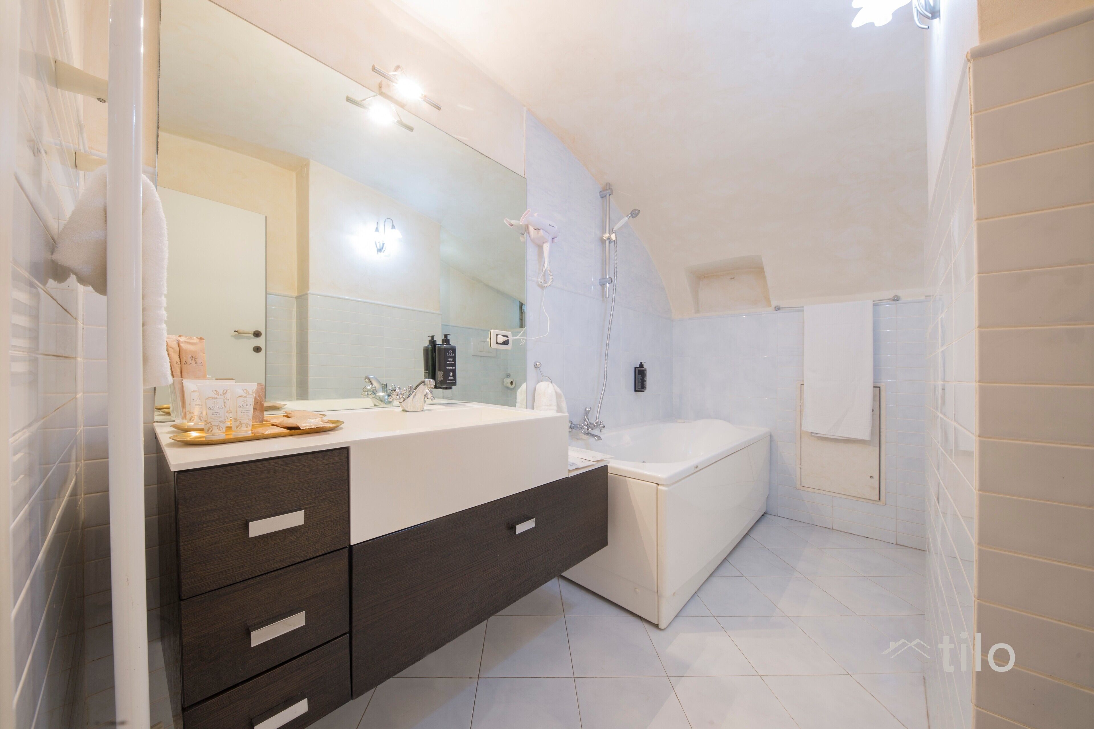 A modern bathroom with a large mirror, a bathtub, and a vanity with drawers.