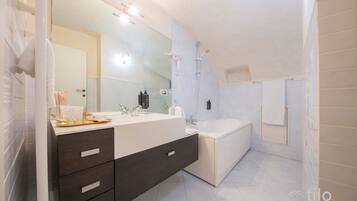 A modern bathroom with a large mirror, a bathtub, and a vanity with drawers.