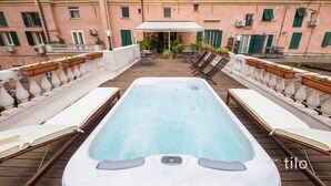 Une piscine sur le toit, agrémentée de chaises longues et de jardinières, entourée d’un bâtiment rose aux volets verts.