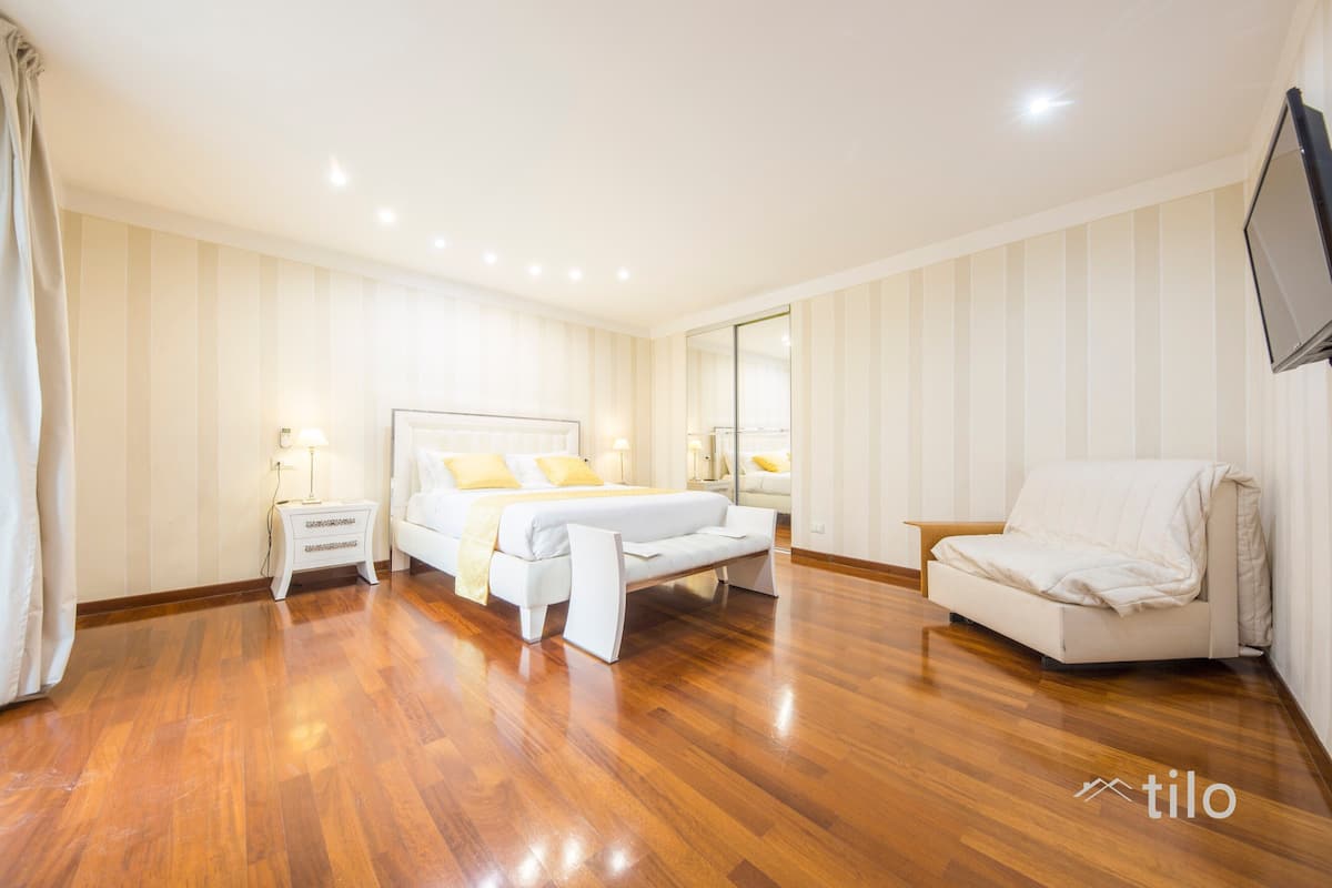 A spacious bedroom with a large bed, bedside tables, a chair, and a TV.