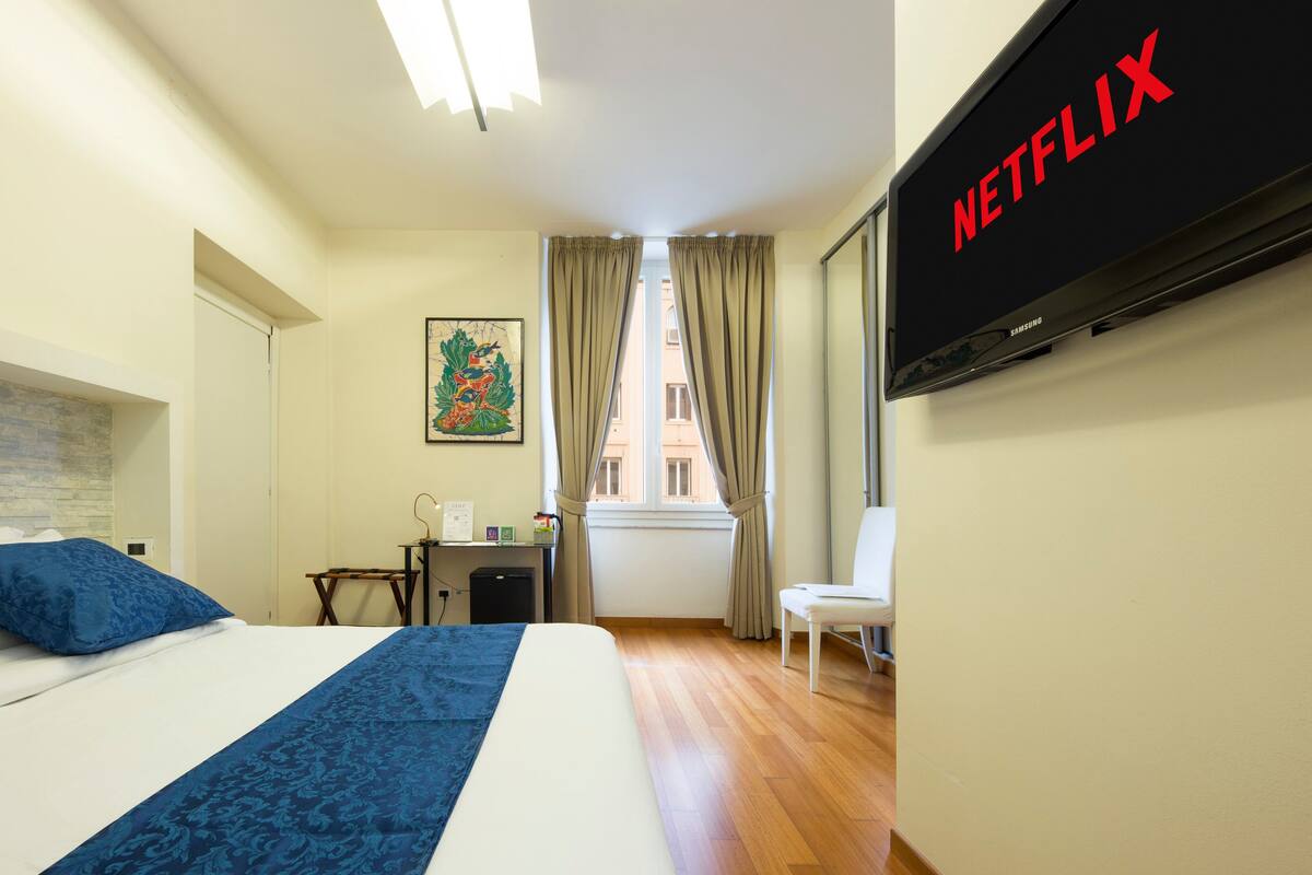 A hotel room with a bed, a desk, a chair, a TV, and a window with curtains.