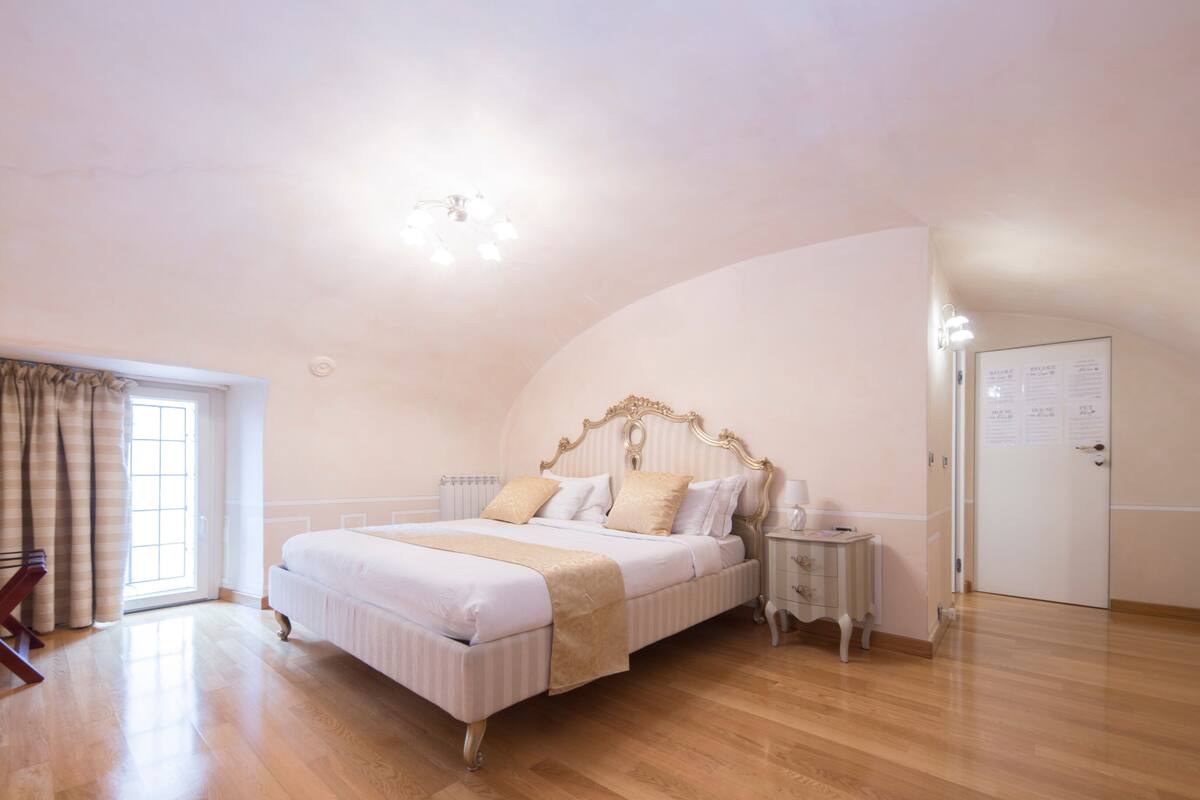 A bedroom with a large bed, a bedside table, a lamp, and a door with a sign.