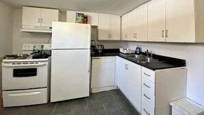 Eine kleine Küche mit weißen Schränken, einem Kühlschrank, einem Herd und einem Geschirrspüler.