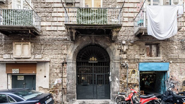 A building with a black arched entrance, a balcony with a metal railing, and a motorcycle parked in front. - Naples Luxury Apartment, located in the historic center of Naples (Napoli)