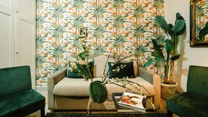 A living room with a floral wallpaper, a sofa, two green armchairs, a coffee table with a magazine, and a potted plant. - Naples Luxury Apartment, located in the historic center of Naples (Napoli)