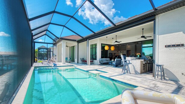 A swimming pool with clear water, surrounded by lounge chairs and a covered patio area. - VRCC - Villa Taradise (Cape Coral)