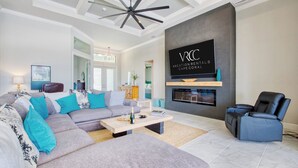 A modern living room with a sectional sofa, a fireplace, and a mounted TV. - VRCC - Villa Taradise (Cape Coral)