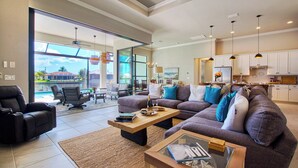 A spacious living room with a large sofa, a coffee table, and a view of a pool and outdoor area. - VRCC - Villa Taradise (Cape Coral)