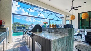 A modern kitchen with a large island, outdoor pool, and a view of the sky. - VRCC - Villa Taradise (Cape Coral)