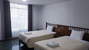A hotel room with two beds, a wooden headboard, a nightstand, and a window with curtains. - HOTEL HAYLLI INN (Arequipa)