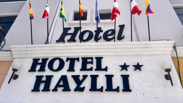A hotel sign with multiple flags and the name "HOTEL HAYLLI" prominently displayed. - HOTEL HAYLLI INN (Arequipa)