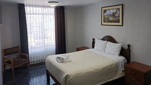 A hotel room with a bed, a chair, a nightstand, a picture on the wall, and a window with curtains. - HOTEL HAYLLI INN (Arequipa)