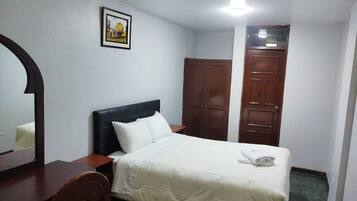 A hotel room with a bed, a wooden wardrobe, a nightstand, a mirror, and a framed picture on the wall.