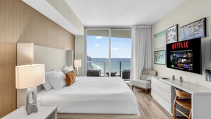 A hotel room with a bed, bedside lamps, a desk, a chair, a TV, and a view of the ocean. - Bright & Stylish Stay at Splendid Resort - Prime Location and Stunning Views (Hollywood)