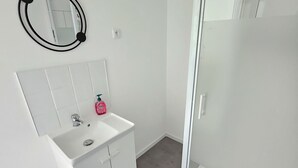A modern bathroom with a white vanity, a round mirror, and a glass-enclosed shower.