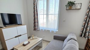A modern living room with a sofa, a coffee table, a TV on a wooden cabinet, and a window with sheer curtains.