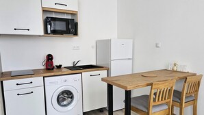 A compact kitchen with white cabinetry, a microwave, a washing machine, and a refrigerator. There's a wooden table with two chairs.