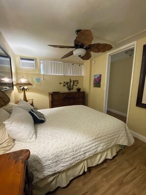 A bedroom with a bed, a ceiling fan, a dresser, a lamp, and a window with blinds.