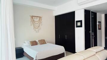 Une chambre comprenant un lit, une armoire, un coin salon et une décoration murale en macramé.