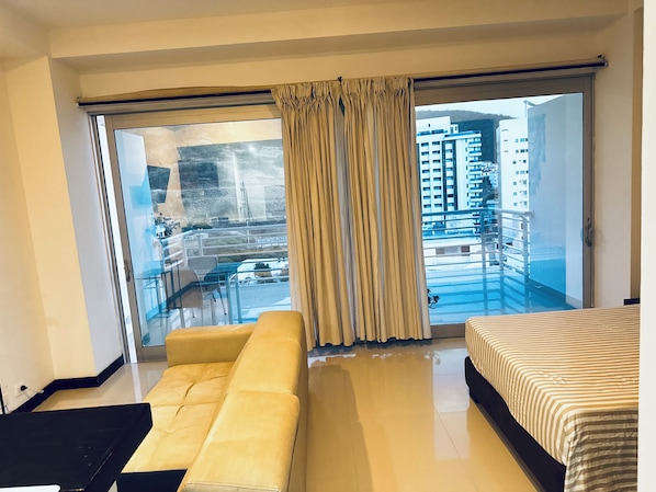 A hotel room with a sofa, a bed, and a balcony with a view of buildings.