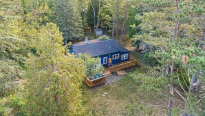 A cabin surrounded by dense forest, with a wooden deck and a chimney. - Wooded Retreat across from Lake MI (Manistee)