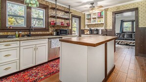 A kitchen with white cabinets, a wooden island, a microwave, and a ceiling fan. - Wooded Retreat across from Lake MI (Manistee)