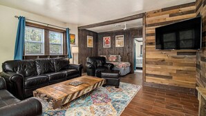 A living room with a leather sofa, a coffee table, and a TV mounted on a wooden wall. - Wooded Retreat across from Lake MI (Manistee)