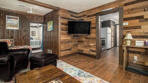 A living room with a wooden wall, a flat-screen TV, a sofa, and a coffee table. - Wooded Retreat across from Lake MI (Manistee)